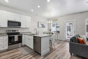Modern kitchen featuring white cabinetry, granite countertops, and stainless steel appliances, including a microwave, range, and dishwasher