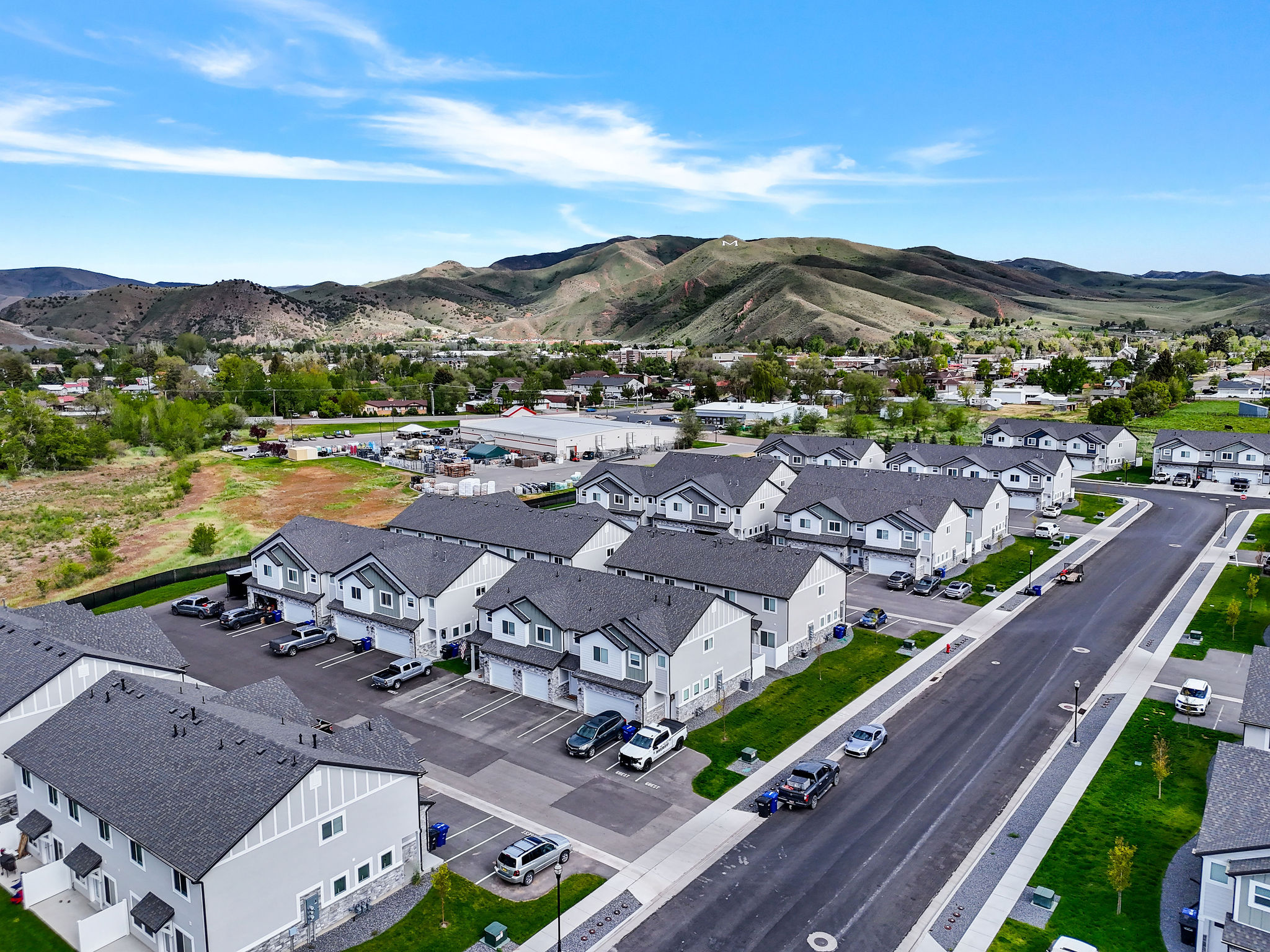 A collection of modern townhomes featuring light gray siding with dark gray gables, dark shingle roofing, and integrated garages, situated with a backdrop of distant mountains