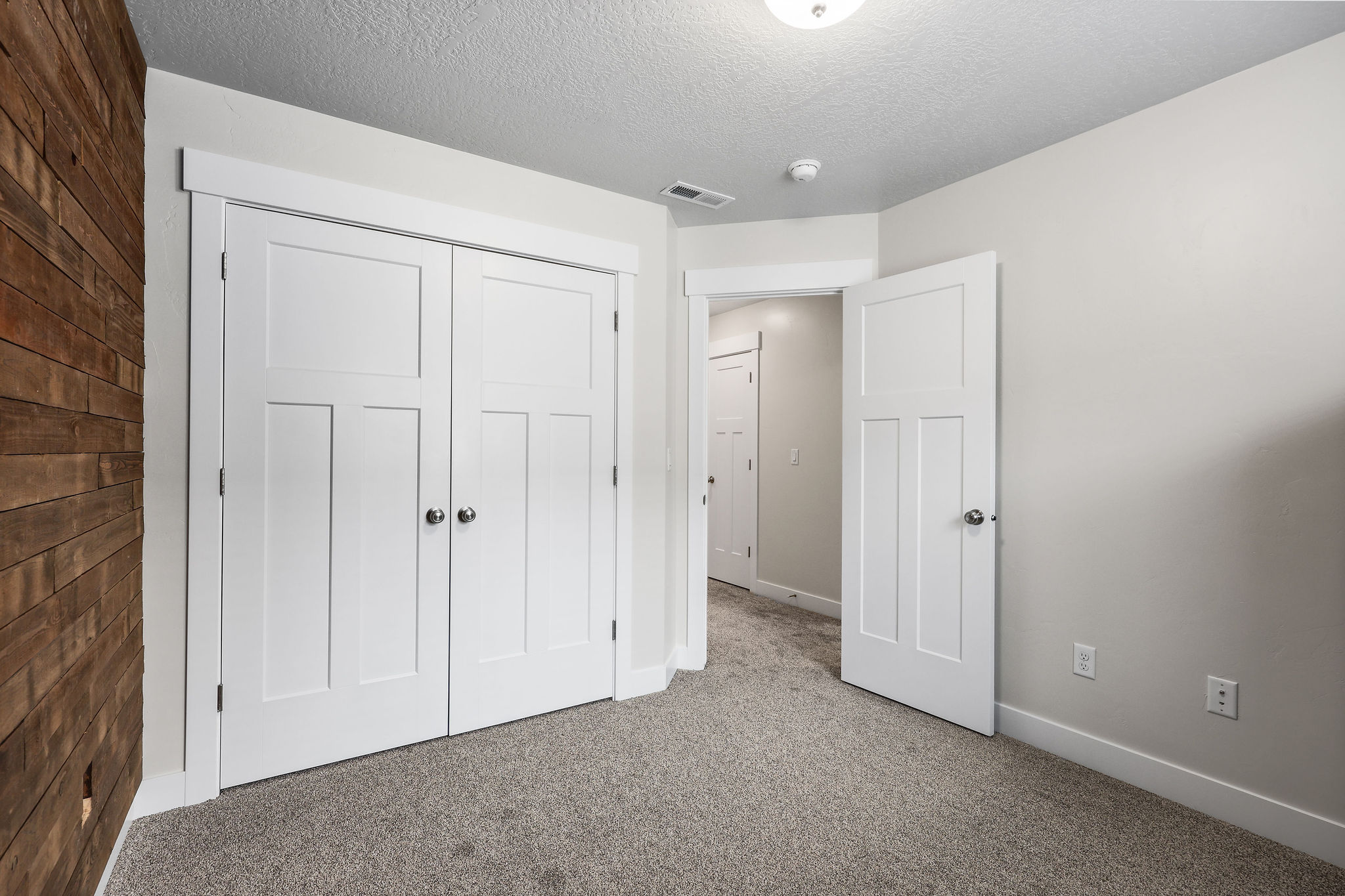 Bedroom featuring a wood accent wall, white paneled doors, neutral gray carpet, and light gray wall paint