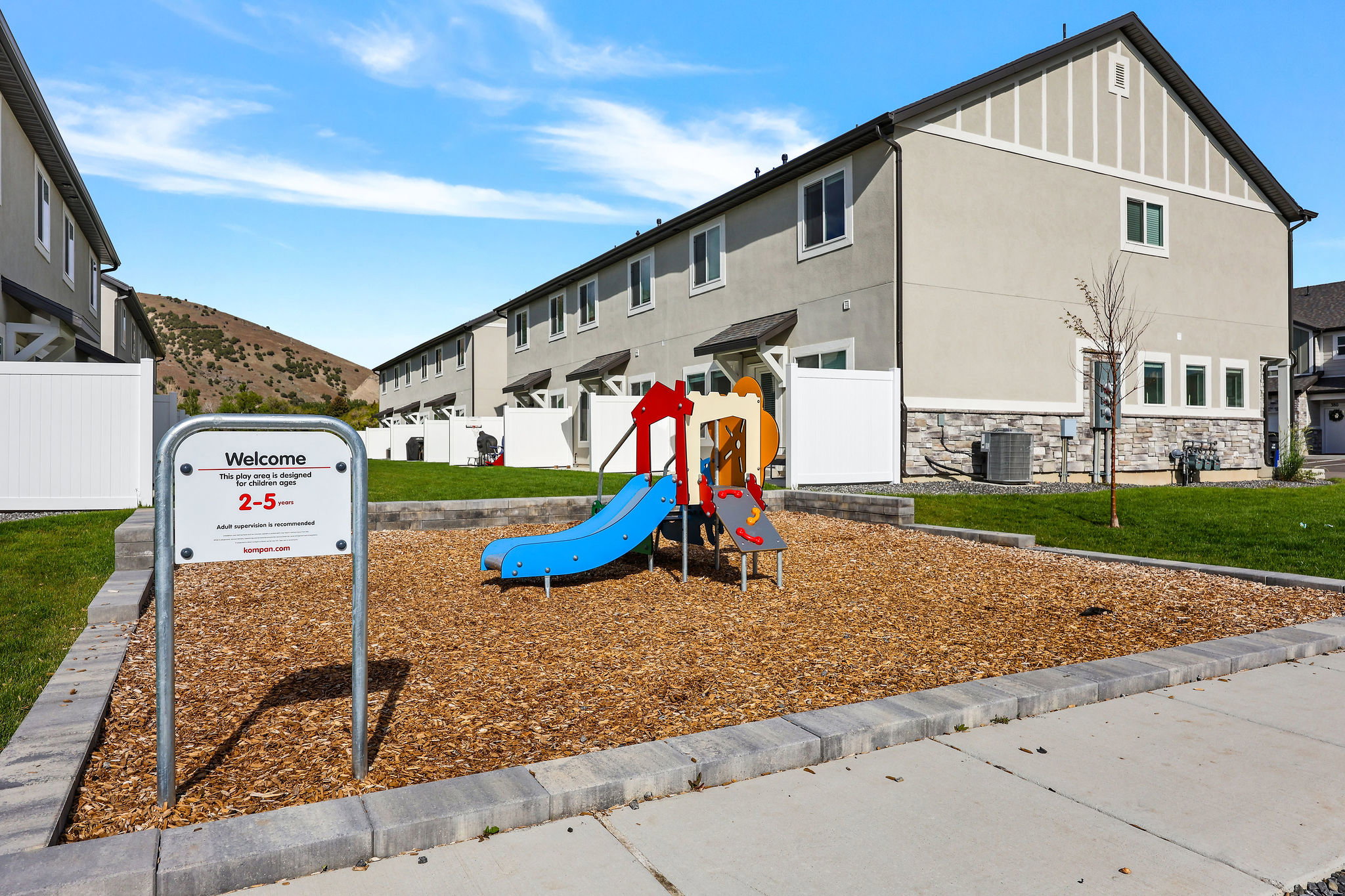Community playground featuring a colorful playset on wood chip surfacing, bordered by a concrete block retaining wall