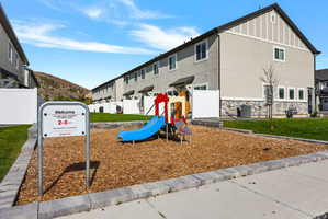 Community playground featuring a colorful playset on wood chip surfacing, bordered by a concrete block retaining wall