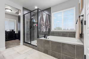 Bathroom featuring a built-in soaking tub with dark gray tile surround, a glass-enclosed shower with black trim, and light-toned tile flooring