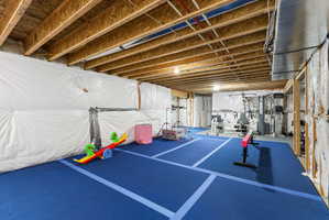Spacious unfinished basement featuring exposed ceiling joists and blue carpet flooring with light blue accent stripes