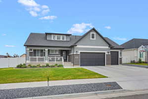 Contemporary ranch-style residence featuring a gray stucco and brick exterior, an inviting covered front porch with white railings, a three-car garage, and a concrete driveway