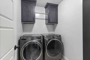 Dedicated laundry area featuring overhead dark wood-finish cabinetry with crown molding, a stainless steel hanging rod, and light gray painted walls