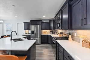 Open-concept kitchen featuring dark wood cabinetry, light countertops, stainless steel appliances, a tile backsplash, and wood-finish flooring