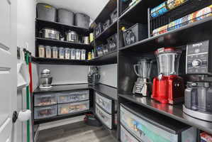 Walk-in pantry featuring extensive built-in shelving, durable dark countertops, wood-finish flooring, integrated wall storage, and a white interior door
