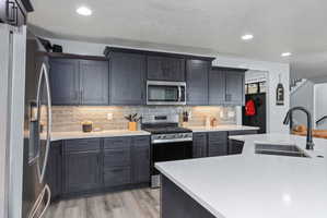 Modern kitchen featuring dark wood-finish cabinetry, light-toned countertops, a subway tile backsplash, stainless steel appliances, and wood-finish flooring