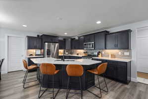 Contemporary kitchen featuring dark cabinetry, stainless steel appliances, a center island with seating, a subway tile backsplash, and recessed lighting