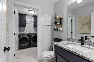 Dedicated laundry area with upper cabinetry and a hanging rod, accessible from a bathroom featuring a dark vanity with a speckled countertop, undermount sink, and black faucet
