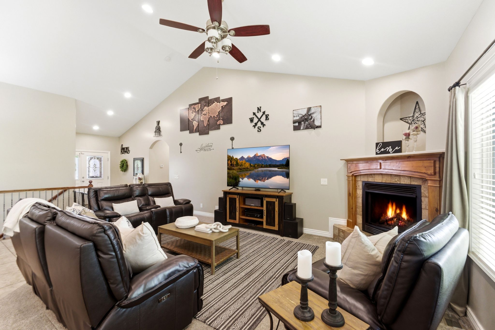 Spacious living area featuring a vaulted ceiling with recessed lighting and a ceiling fan, a fireplace with a wood mantel and stone surround, and large windows with blinds