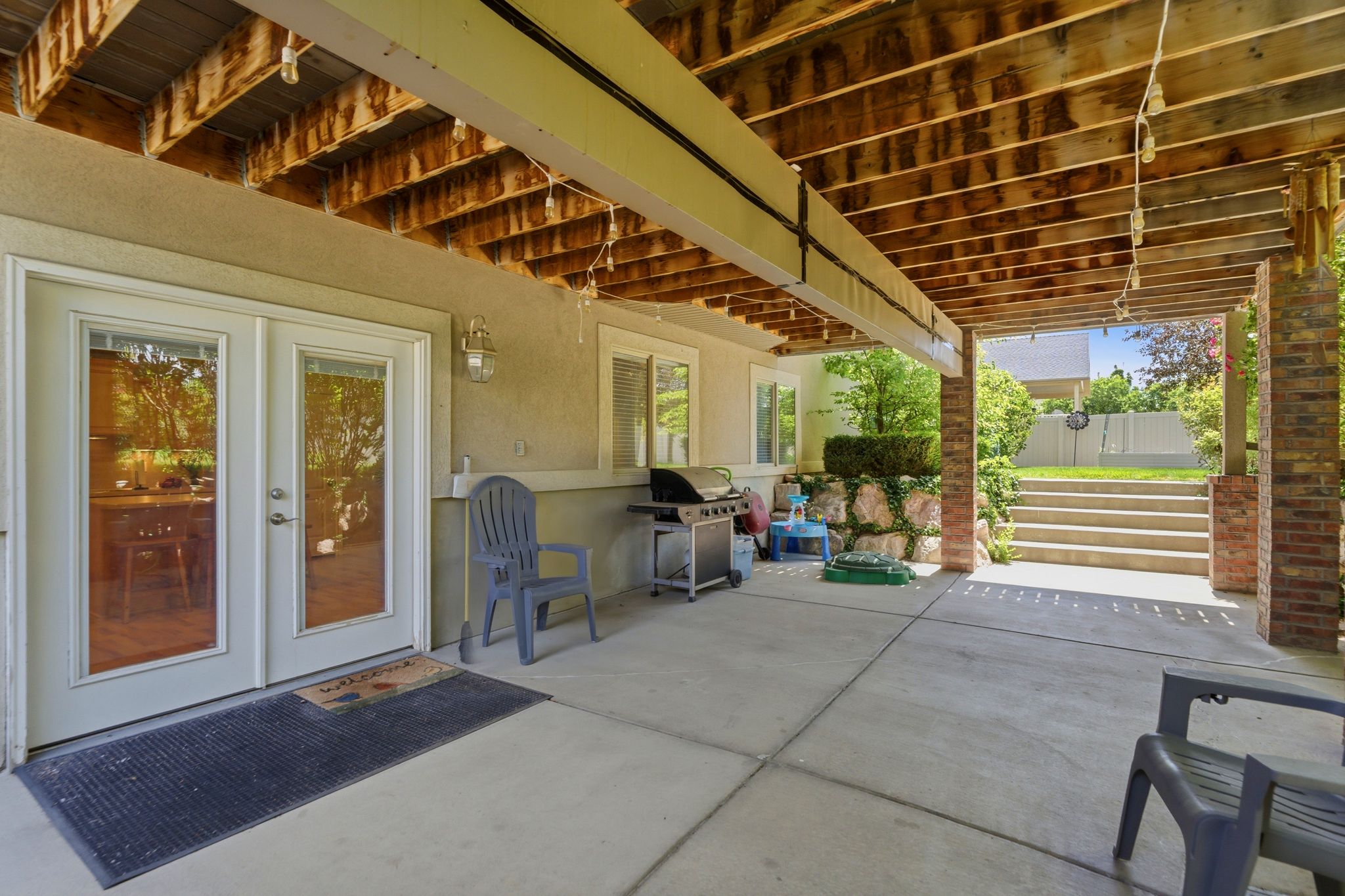 Covered concrete patio featuring exposed wood ceiling joists and brick columns