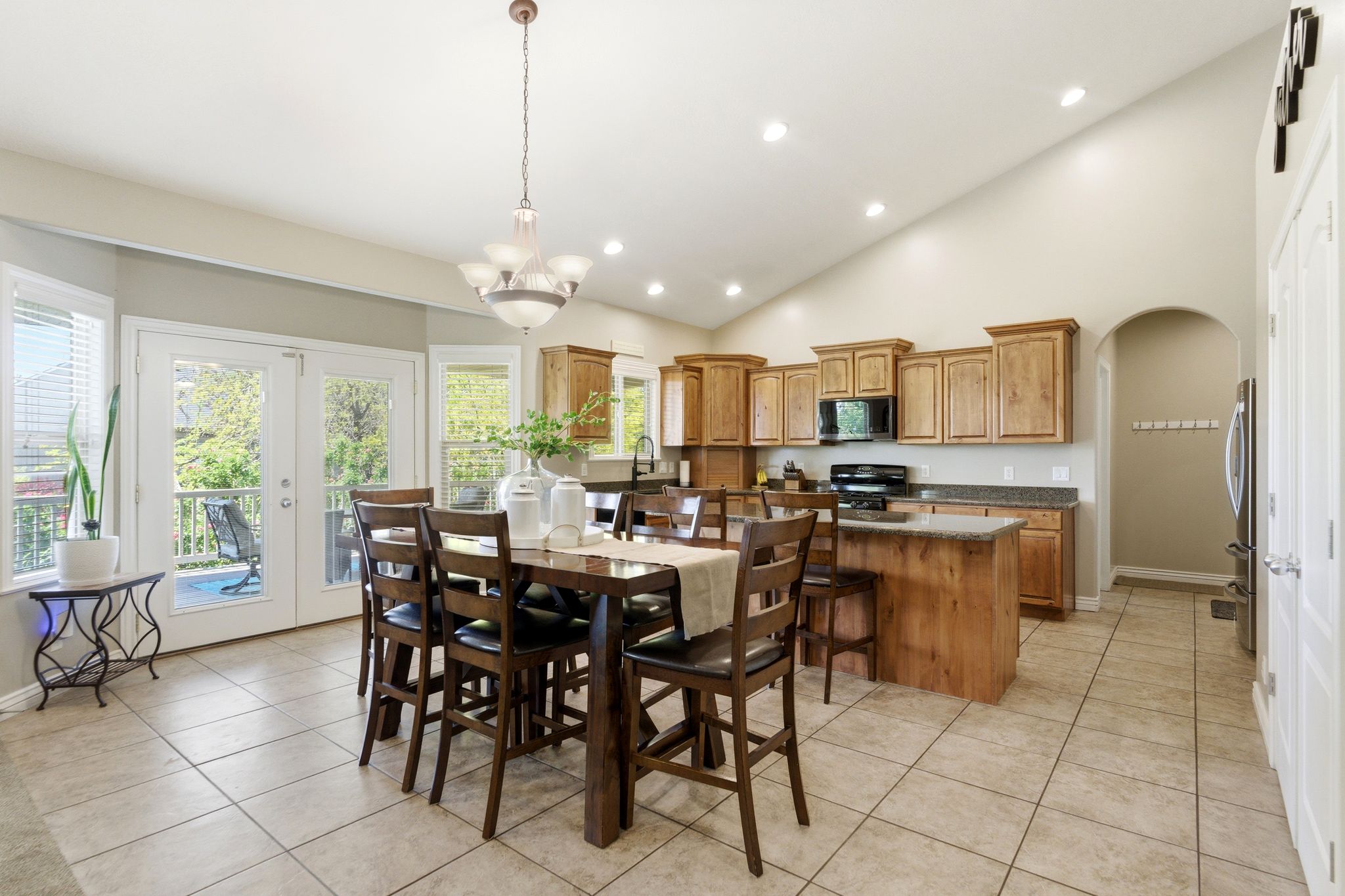 Open-concept kitchen and dining area featuring vaulted ceilings, recessed lighting, double glass patio doors, wood cabinetry, and a kitchen island with stone countertops