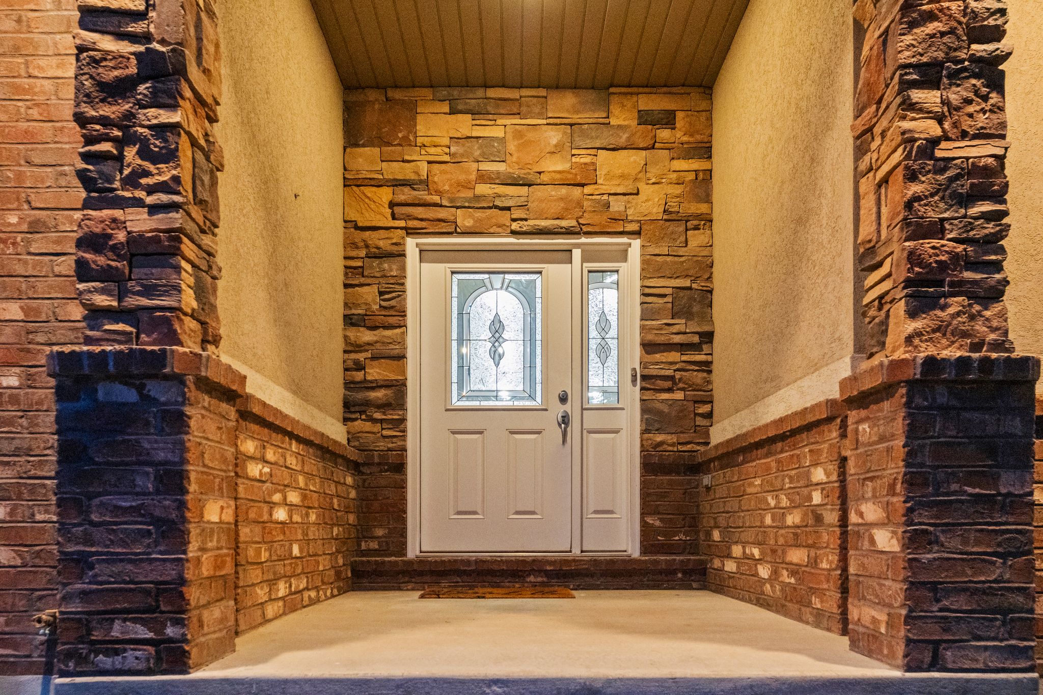 Entryway featuring a white door with decorative glass, stone veneer, brick detailing, and a stucco finish