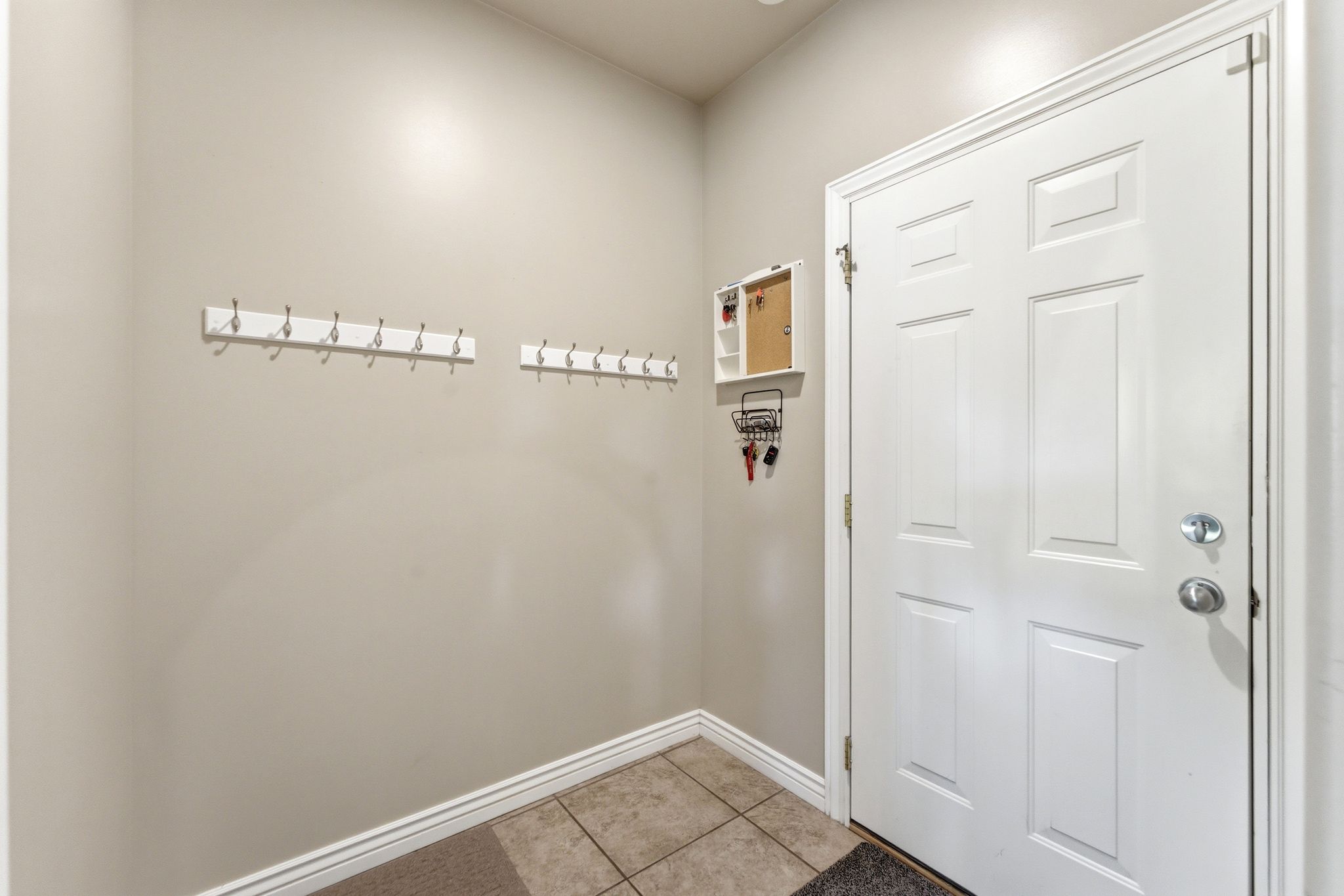 Entryway featuring a white paneled door, ceramic tile flooring, and two wall-mounted coat racks