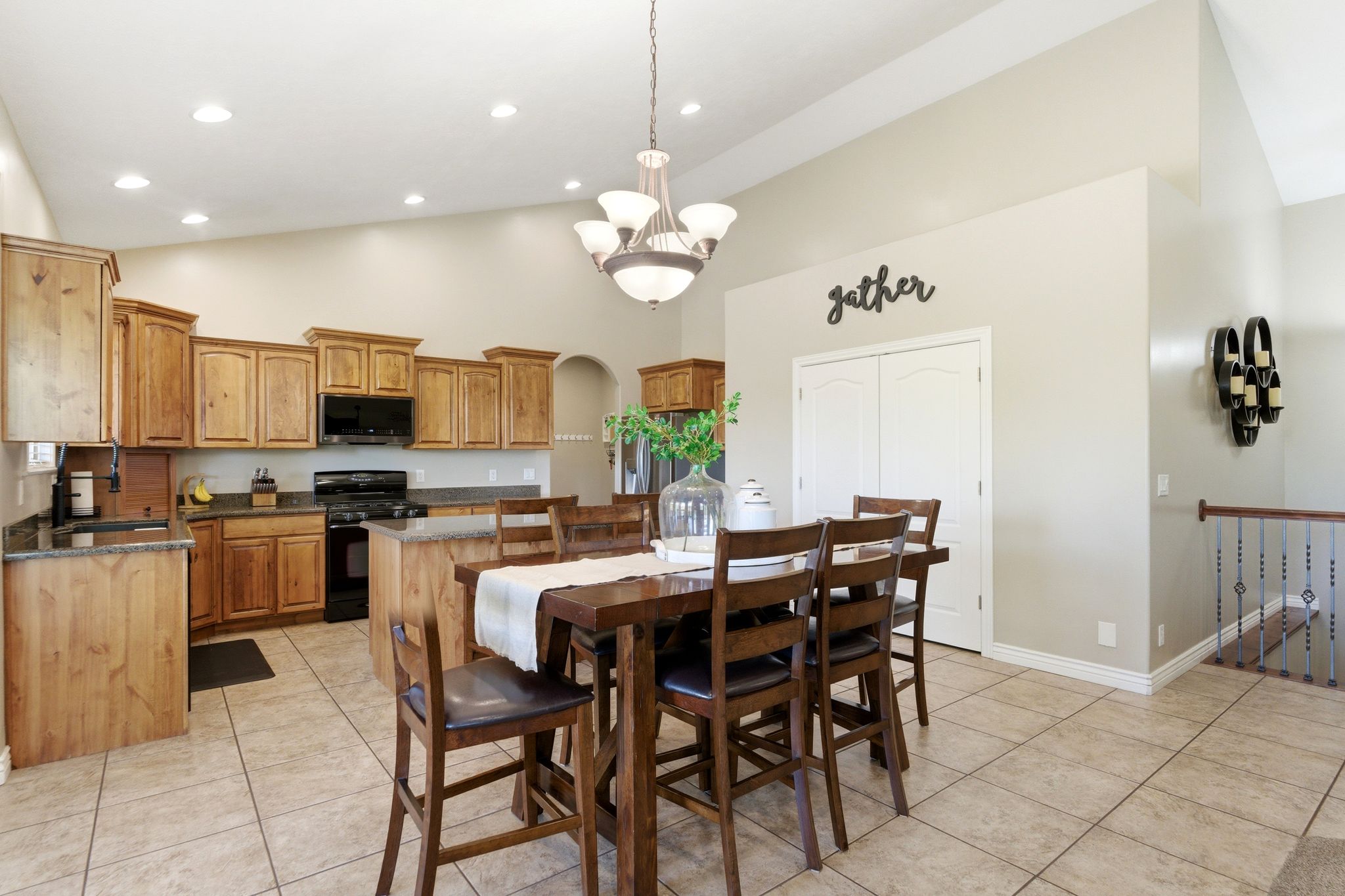 Open-concept kitchen and dining area featuring vaulted ceilings, recessed lighting, wood cabinetry, dark countertops, and tile flooring