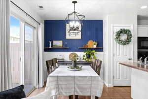 Dining area featuring a modern geometric chandelier, a deep blue accent wall with wainscoting, and wood-finish flooring