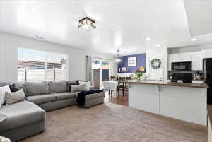 Open-concept living area featuring soft carpet flooring, recessed lighting, and a large window with horizontal blinds