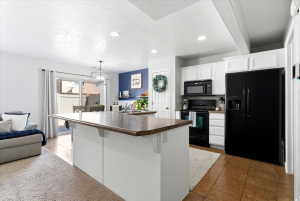 Kitchen featuring an island with a breakfast bar, white cabinetry, black appliances, and tile flooring