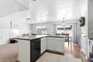 Open-concept living space featuring a central island with a dishwasher, white cabinetry, a kitchen sink, and brown countertops
