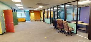 Open concept office space featuring modular glass-paneled walls and a neutral carpeted floor