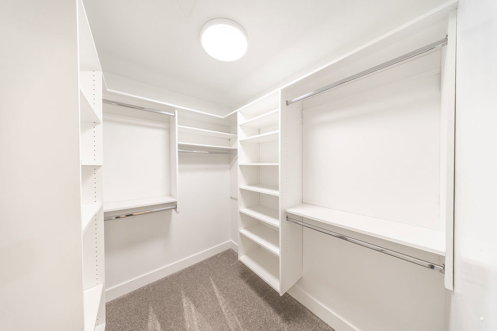 Walk-in closet featuring white built-in shelving, multiple hanging rods, and recessed lighting