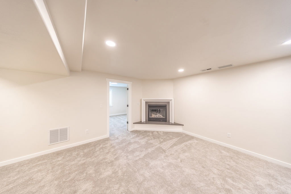 Spacious room featuring a corner fireplace with a dark surround and hearth, neutral-toned carpet, recessed lighting, and white baseboards