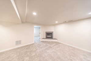 Spacious room featuring a corner fireplace with a dark surround and hearth, neutral-toned carpet, recessed lighting, and white baseboards