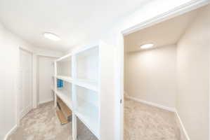 Spacious walk-in closet featuring white built-in shelving, plush carpeting, and recessed lighting