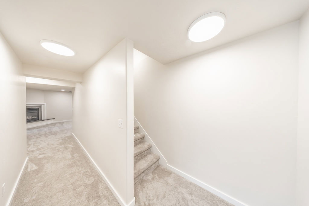 Carpeted stairs leading to a lower level featuring recessed lighting, a fireplace with a mantel, and light-colored walls and carpeting