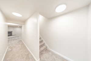 Carpeted stairs leading to a lower level featuring recessed lighting, a fireplace with a mantel, and light-colored walls and carpeting