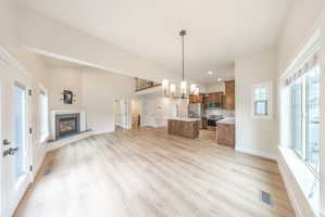 Spacious open-concept interior featuring light wood-finish flooring, a white-mantled fireplace with a dark surround, and vaulted ceilings