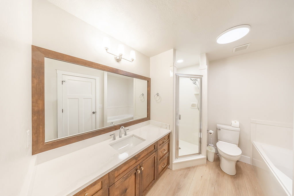 Bathroom featuring a wood-finish vanity with a light-colored countertop, an undermount sink, and a large framed mirror