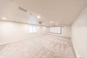 Expansive media room featuring a large projection screen, mounted projector, recessed lighting, patterned carpet, and a window with blinds