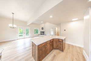 Spacious open concept interior featuring a large kitchen island with wood-finish cabinetry and light-toned countertop, wood-finish flooring, a vaulted ceiling, and a fireplace with a light-toned hearth