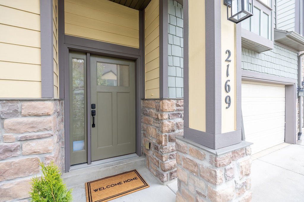 Exterior entry with a paneled door and sidelight, complemented by horizontal siding and stone veneer accents