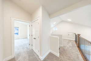 Carpeted hallway featuring a vaulted ceiling, recessed lighting, and a white paneled door