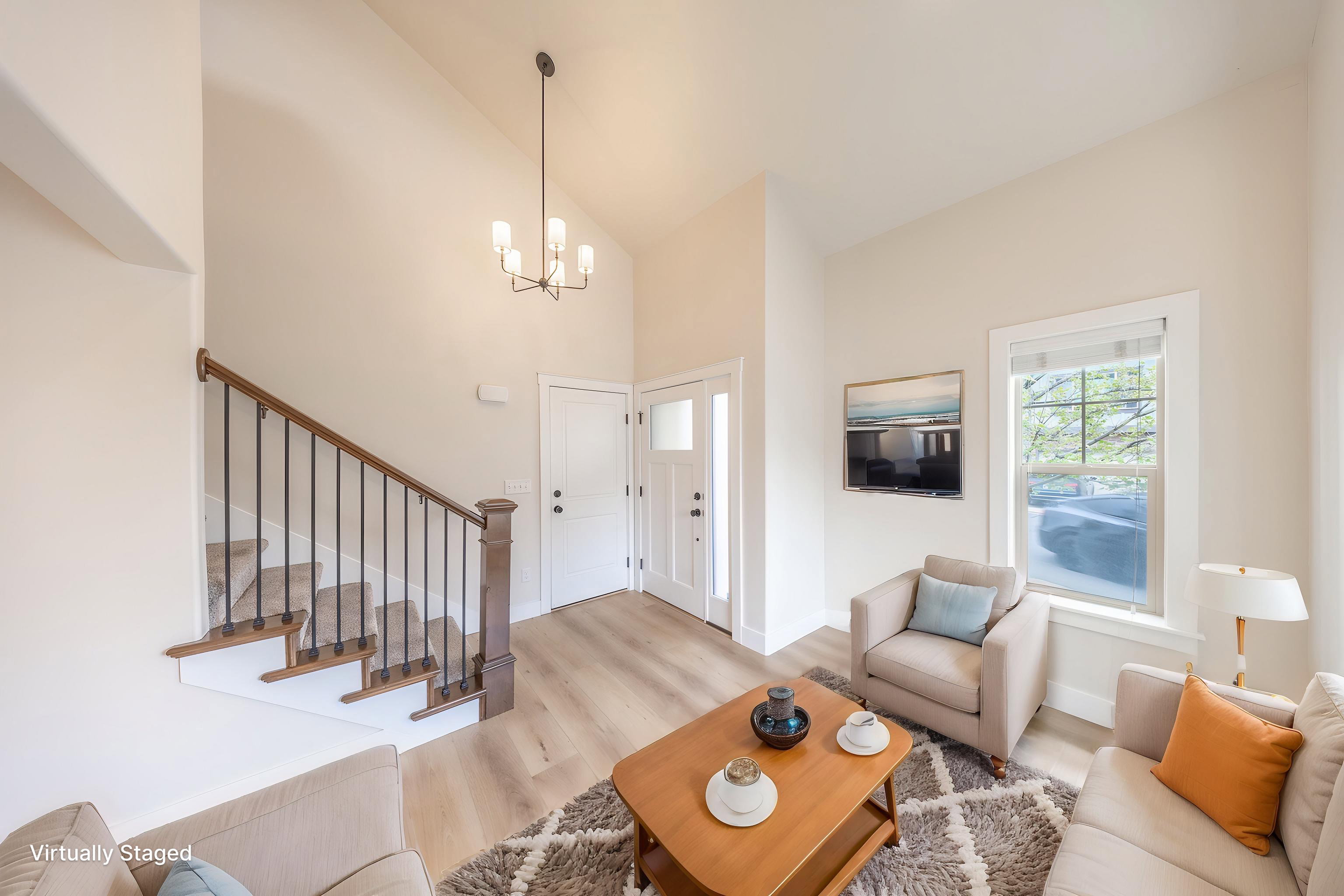 Foyer and living area featuring high ceilings, wood-finish flooring, a contemporary chandelier, a white paneled front door with sidelight, and a staircase with wood newel posts and iron balusters
