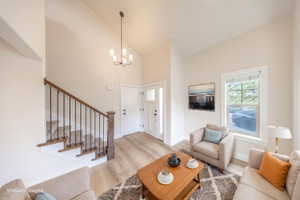 Foyer and living area featuring high ceilings, wood-finish flooring, a contemporary chandelier, a white paneled front door with sidelight, and a staircase with wood newel posts and iron balusters
