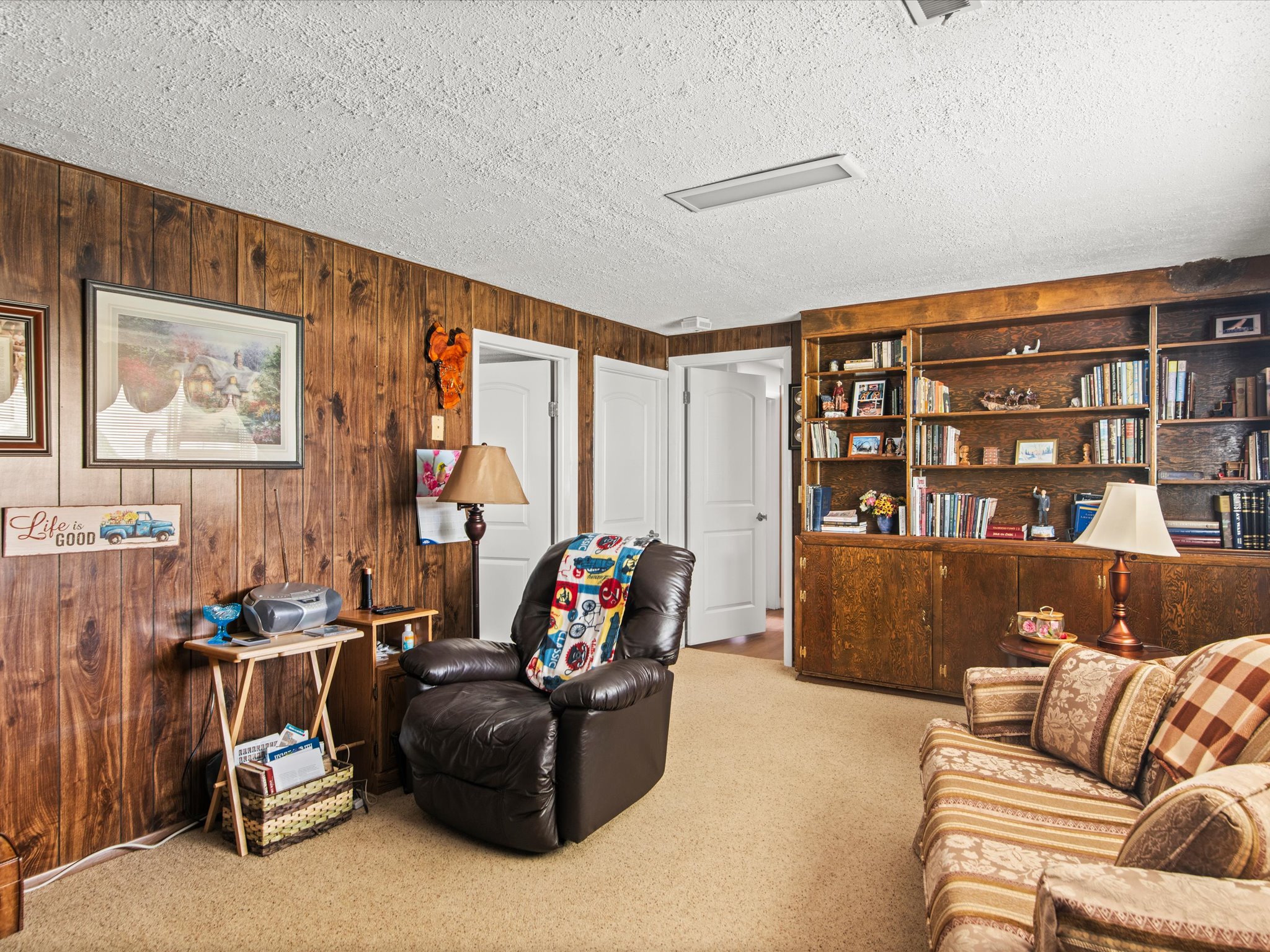 Wood-paneled room featuring extensive built-in shelving, integrated cabinetry, and light-toned carpeting