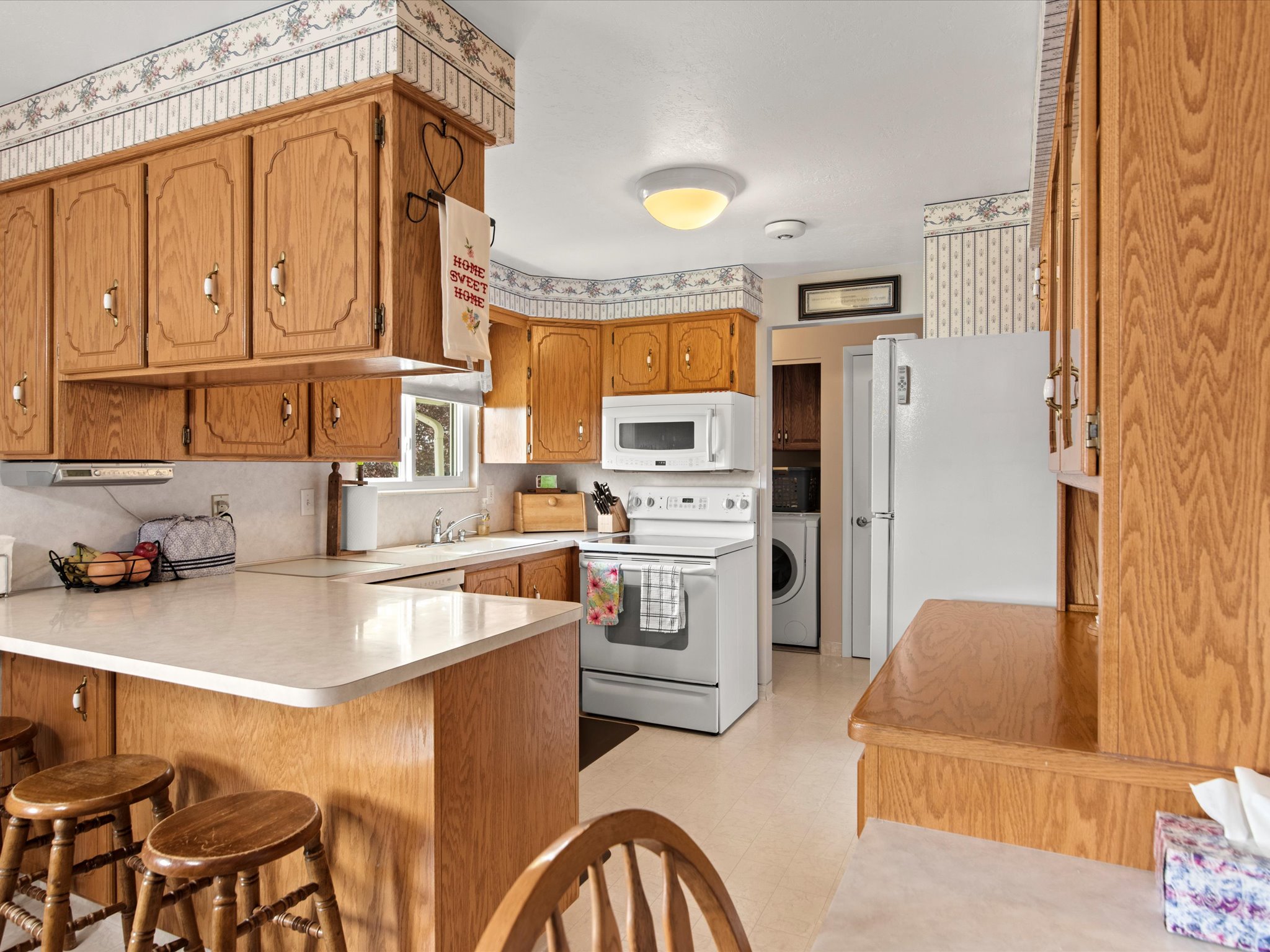 Kitchen featuring light wood cabinetry, white countertops, built-in microwave, white appliances, and a window above the sink