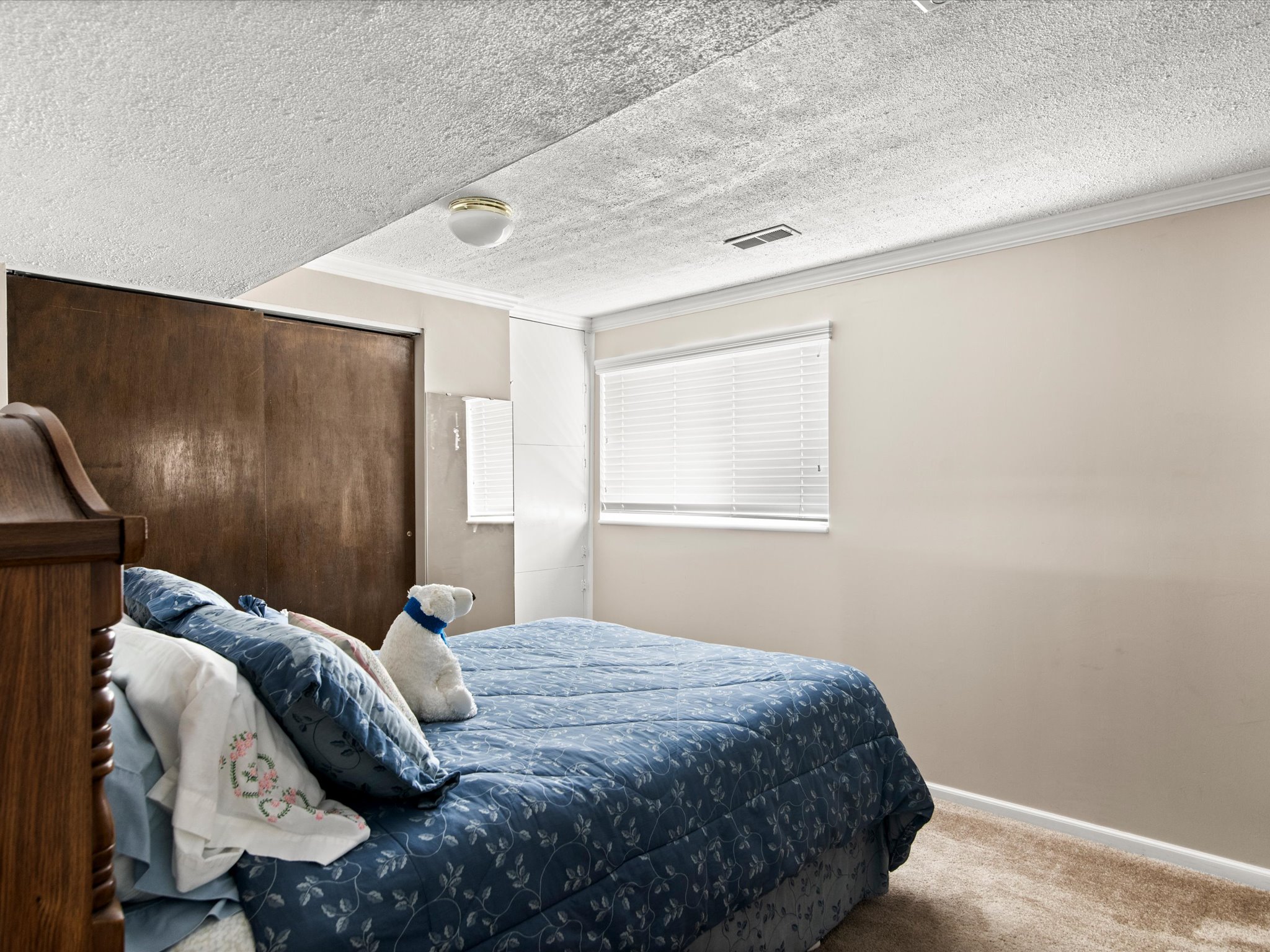Spacious room featuring neutral carpeting, a single window with blinds, and a built-in closet with sliding wood-panel doors