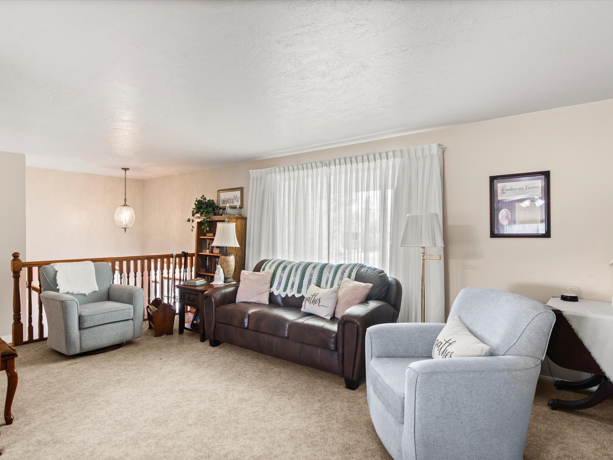 Carpeted living area featuring a wooden railing, white window coverings, and a ceiling-mounted light fixture
