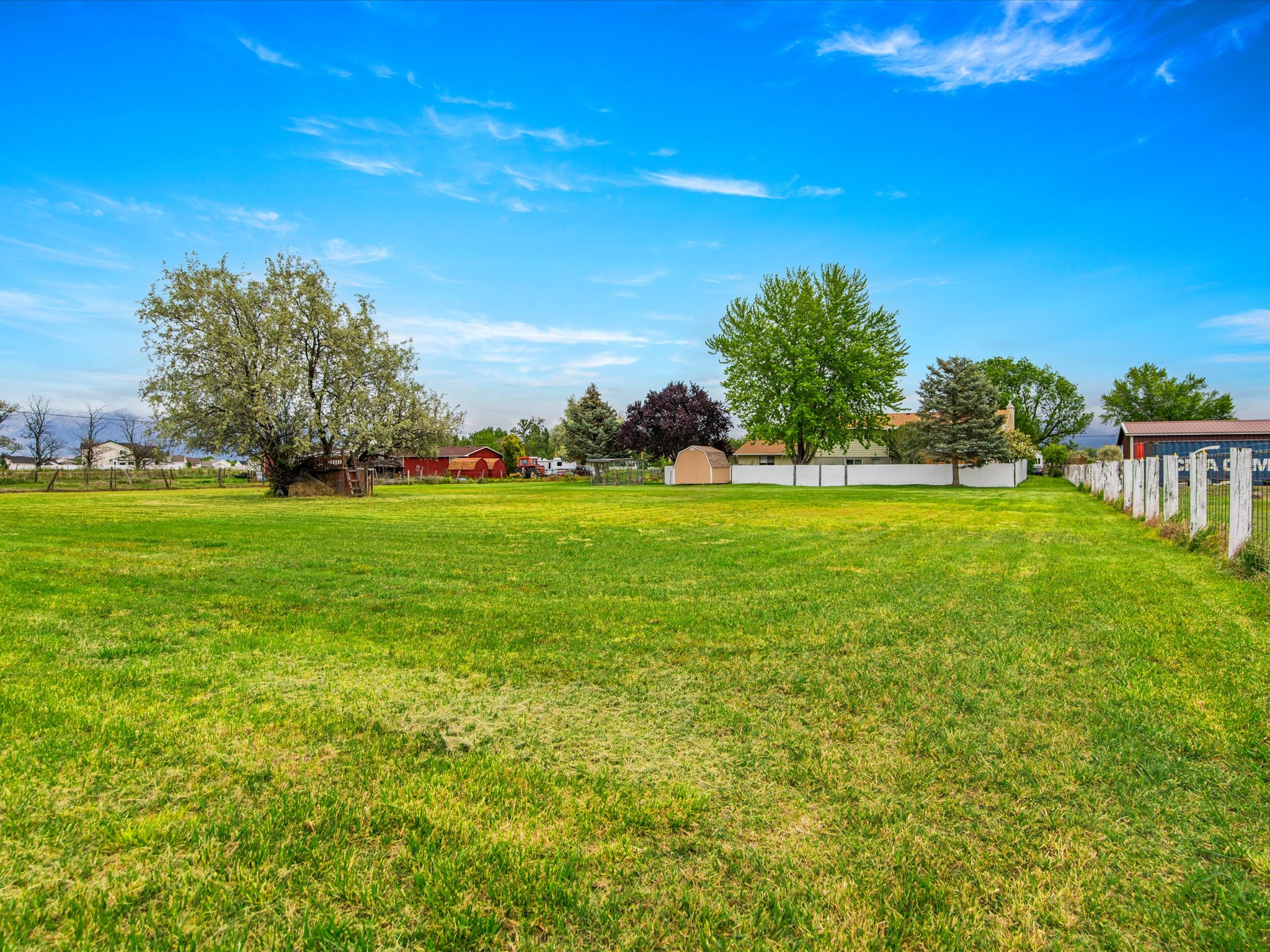 Expansive green lawn with a white post fence and mature trees