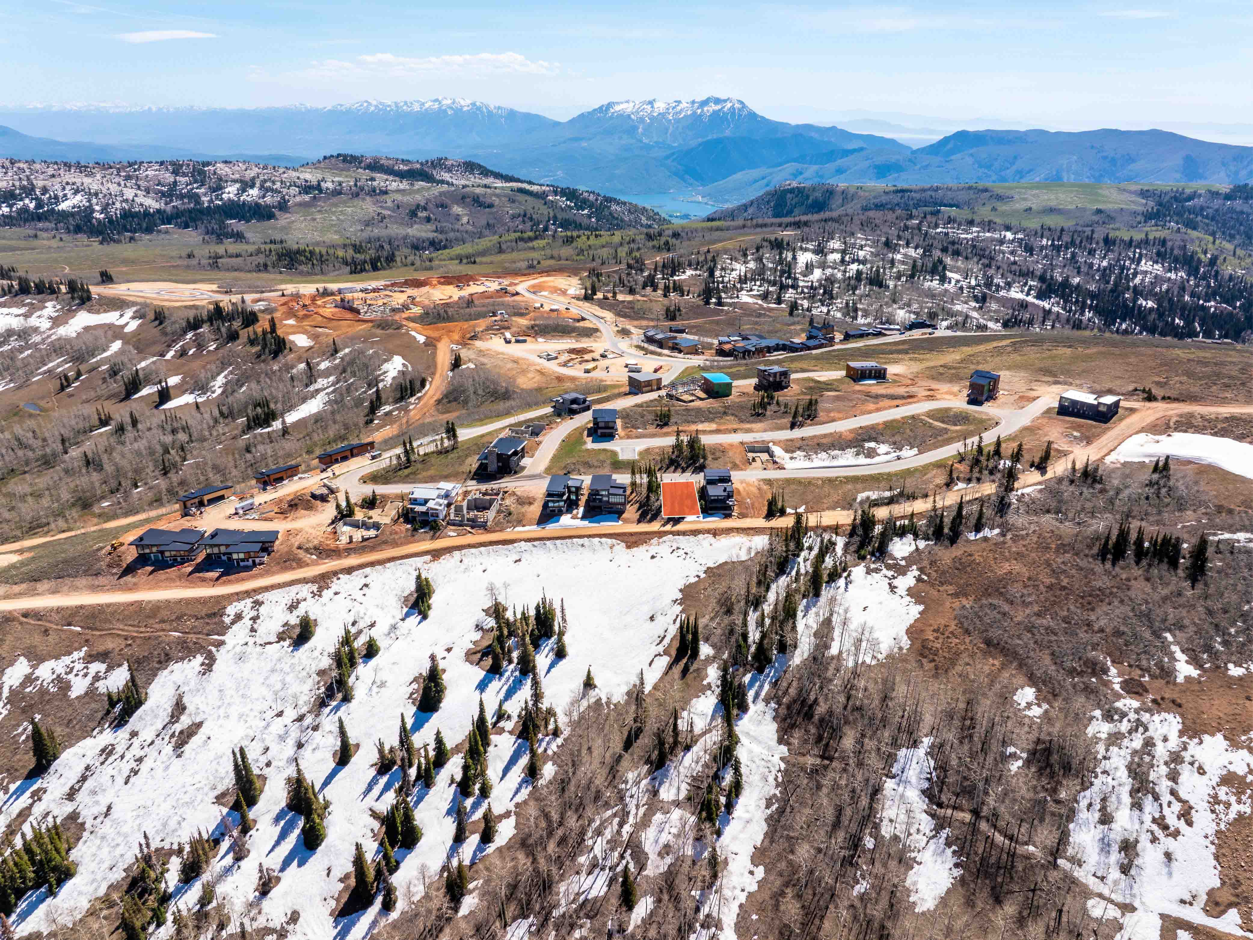 Expansive mountain landscape featuring scattered evergreen and deciduous trees, with snow patches on higher elevations