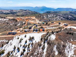 Expansive mountain landscape featuring scattered evergreen and deciduous trees, with snow patches on higher elevations