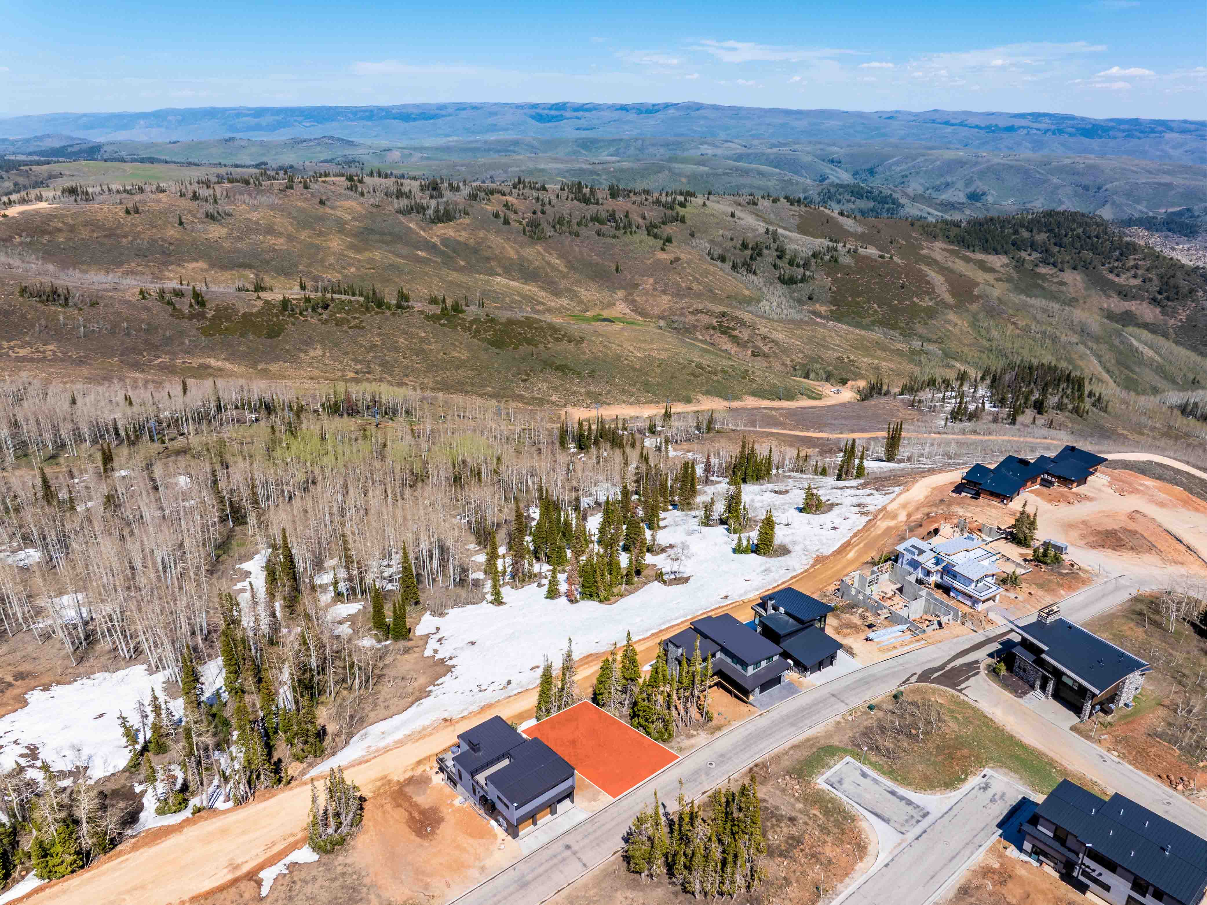 Expansive mountain land featuring a paved road, scattered evergreen trees, and partial snow coverage
