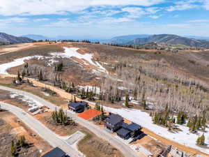 Mountainous terrain with natural snow patches, visible road infrastructure, and surrounding residential structures