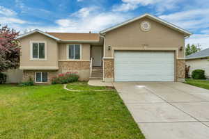 Stucco exterior featuring stone veneer accents, an attached garage, a concrete driveway, and a front lawn with established landscaping
