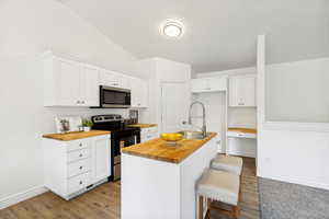 Kitchen featuring white cabinetry, butcher block countertops, stainless steel appliances, and wood-finish flooring